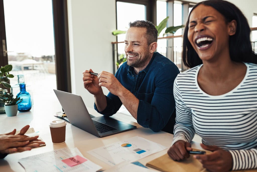 Laughing young African American businesswoman sitting with colleagues around a table during a meeting in an office